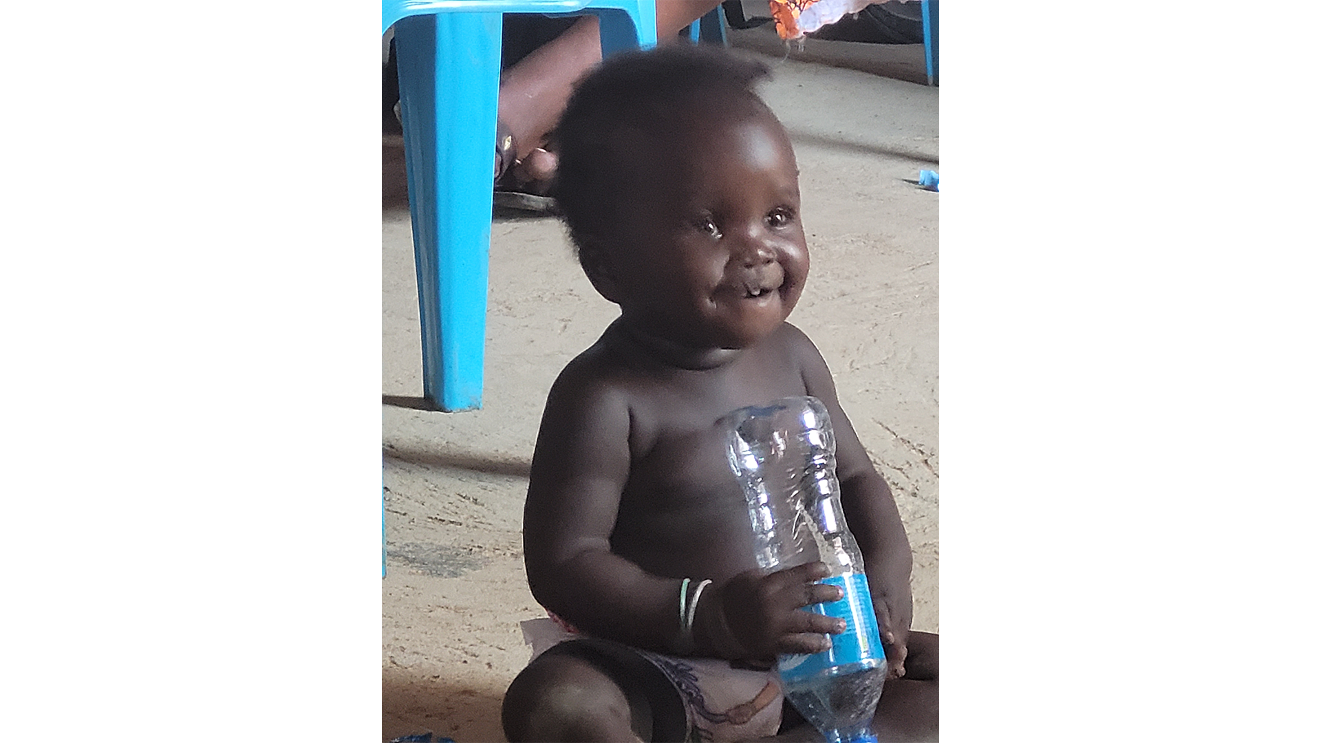 Smiling baby sitting and holding a water bottle